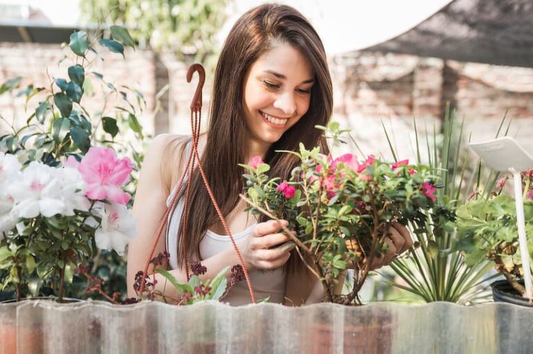 Smiling young woman taking care of flowering plant in the garden.