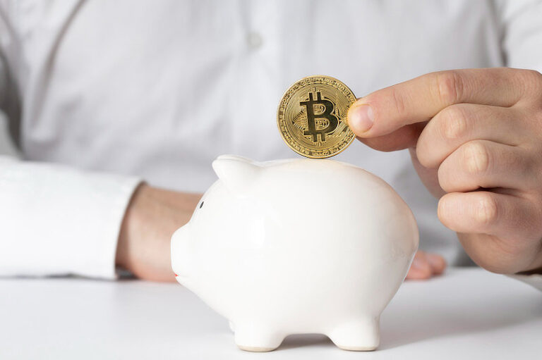 Man inserting a bitcoin in a piggy bank.