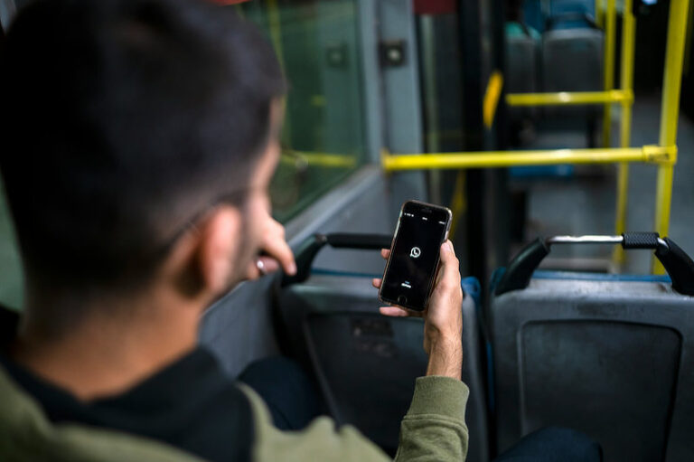 Man sitting in the bus using WhatsApp on iPhone.